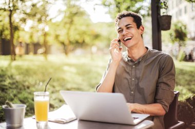 Bir dizüstü bilgisayar ile bir masada oturan ve Smartphone'da konuşurken Afro adam.