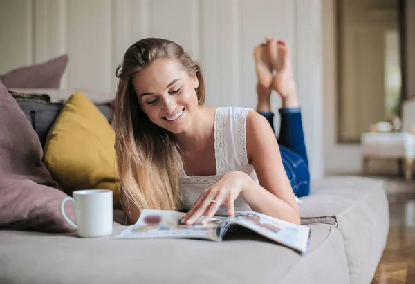 雑誌を読んでベッドで横になっている若い女性 — ストック写真