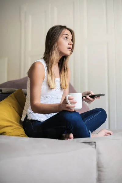 Jovem Sentada Sofá Com Uma Xícara Bebida Smartphone — Fotografia de Stock