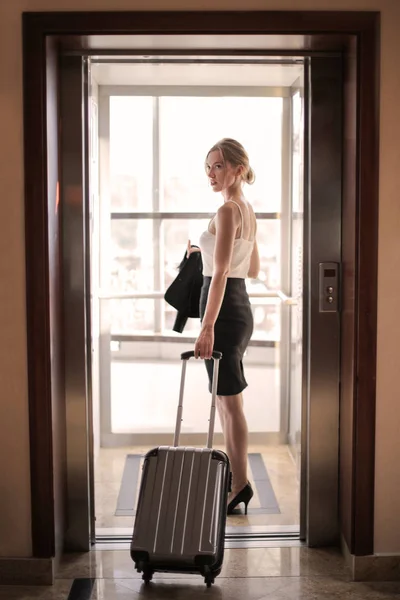 Blonde woman entering a hotel room with luggage.