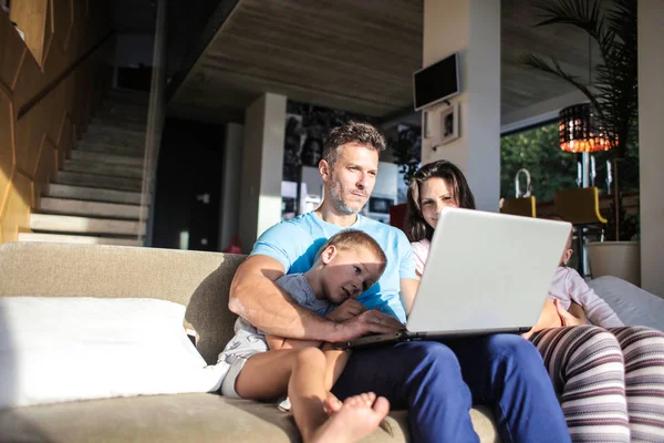 ノート パソコンでリビング ルームに座っている幸せな家族 — ストック写真