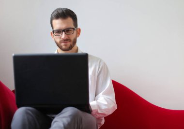 Bir dizüstü bilgisayar ile bir kanepede oturan adam.