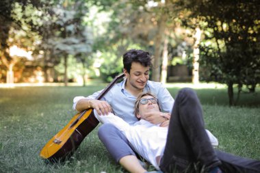 Gay couple lying in the grass in a park.  clipart