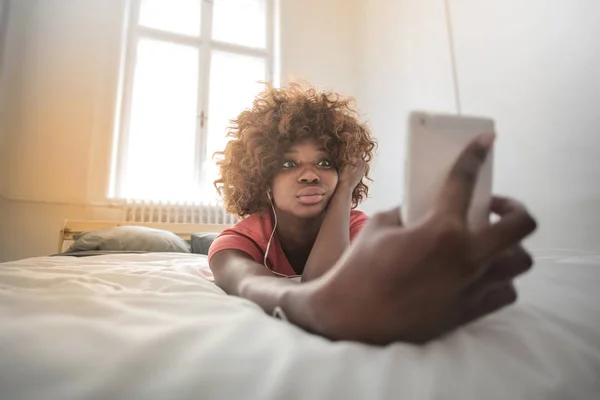 若い黒人女性彼女のベッドで横になっていると Selfie を取って — ストック写真