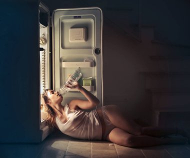 young woman refreshing herself with water at the fridge