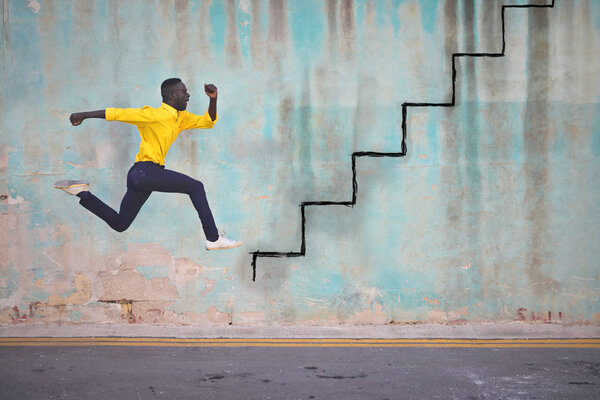 Молодой чёрный мужчина в жёлтой рубашке бежит по лестнице
