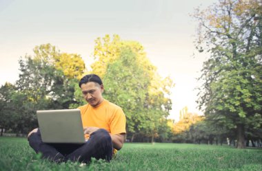 Asya adam çimenlerde oturan ve laptop ile çalışma