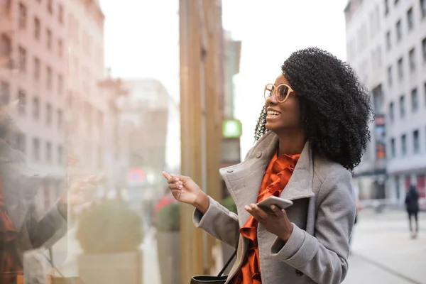 Sonriente Mujer Negra Mirando Los Escaparates Sosteniendo Smartphone — Foto de Stock