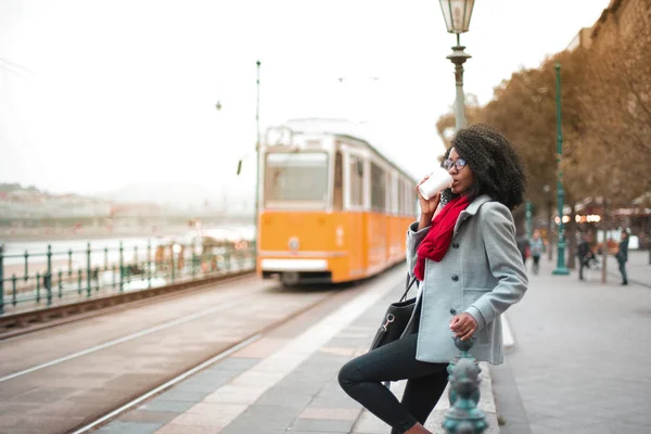 路面電車を待っていると コーヒーを飲んで美しい黒の女の子 — ストック写真