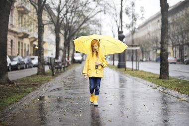 yağmurluk ve şemsiye sokakta yürürken, küçük kız