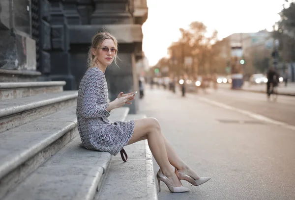 階段で待っている彼女の携帯電話を保持しているサングラスの若い女性 — ストック写真