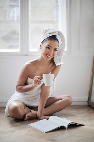 美丽的年轻亚洲妇女在浴袍有咖啡和阅读杂志 — 图库照片