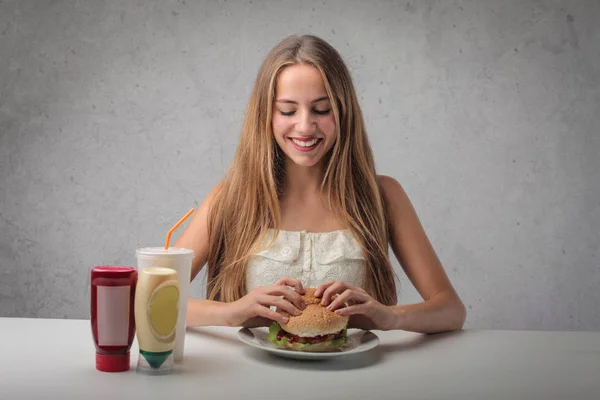 ハンバーガーを食べる若いブロンドの女性 — ストック写真