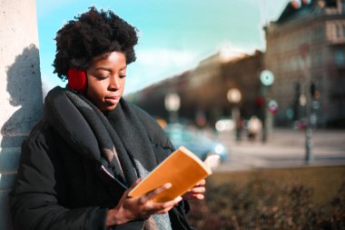 Genç siyah kadın sıcak ceketli bir kitap okuma 