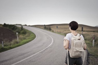 Sırt çantalı genç bir kadın yolda duruyor.