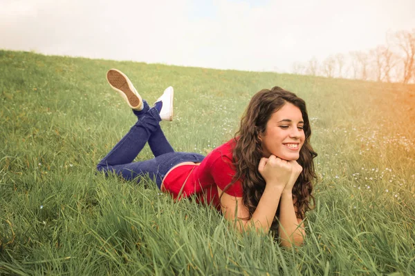 草の中に座っていると笑顔の若いブルネットの女性 — ストック写真