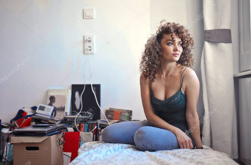 Woman sitting on the bed is looking outside