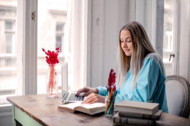 Sarışın kız bir sürü kitap ve dizüstü bilgisayarla çalışıyor.