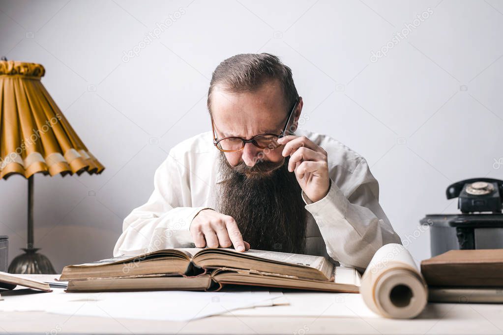 Beared teacher is studying on a big book