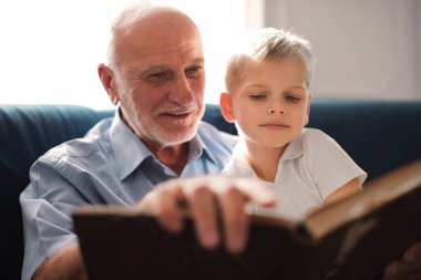 Grandfather and a little boy read on the sofa clipart