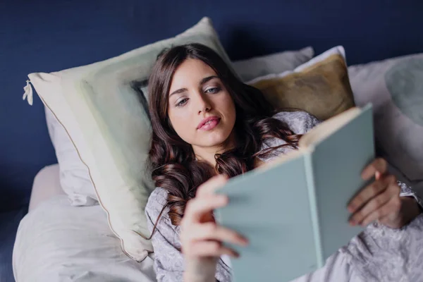 一个女孩躺在床上看书 — 图库照片