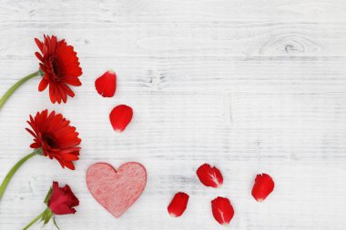 Beyaz ahşap arka planda kırmızı kalpli kırmızı çiçekler.