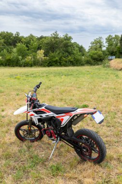 Fransa 'nın Drome kentindeki bir ormanın yakınındaki çimenli bir alana park etmiş kırmızı ve beyaz motosiklet.