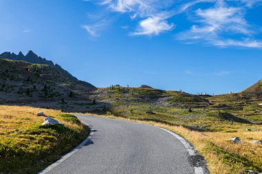 Piedmont 'taki İtalyan Alpleri' nde kayalık dağları ve mavi gökyüzü olan Vinadio yakınlarındaki çayırlardan geçen manzaralı yol.
