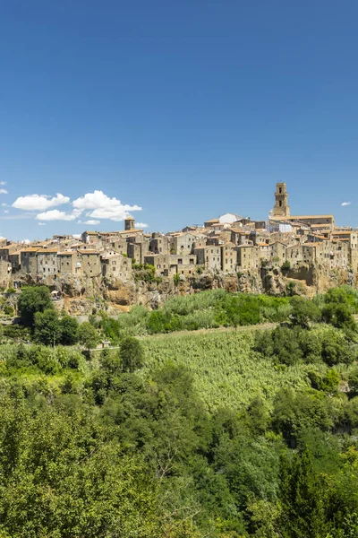 Pitigliano, Tuscany, İtalya 'da bir ortaçağ kasabası, mavi gökyüzünün altında yeşil bir bitki örtüsüyle çevrili bir uçurumun üzerinde duruyor.