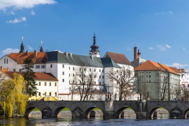 Scenic view of the stone bridge over the Otava River and historical buildings under a blue sky in Pisek, Czechia