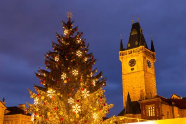 Illuminated Christmas tree with ornaments and lights stands near the Prague Old Town Hall tower