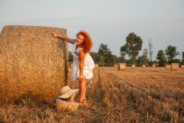 Kızıl saçlı kadın bir saman yığını yakınındaki sahada poz