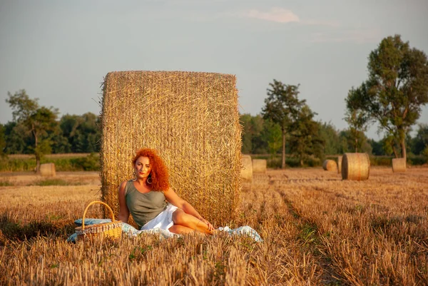 Roodharige vrouw poseren op het veld in de buurt van een stapel hooi — Stockfoto