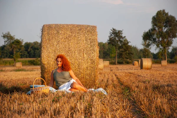 Roodharige vrouw poseren op het veld in de buurt van een stapel hooi — Stockfoto