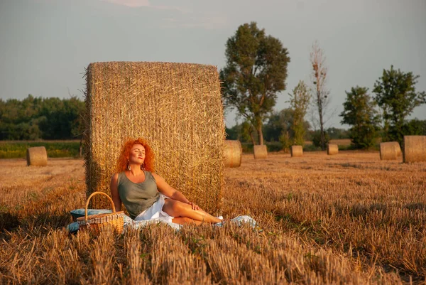 Red-haired woman posing on the field near a hay stack — Stock Photo, Image