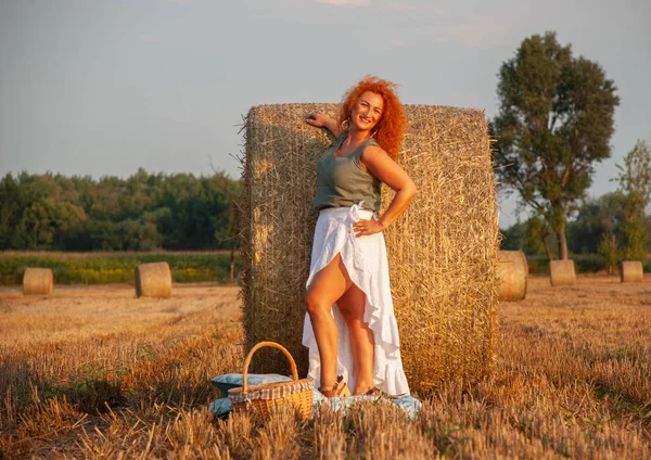 Donna dai capelli rossi in posa sul campo vicino a una pila di fieno — Foto Stock