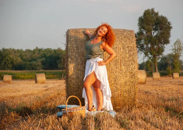 Donna dai capelli rossi in posa sul campo vicino a una pila di fieno — Foto Stock