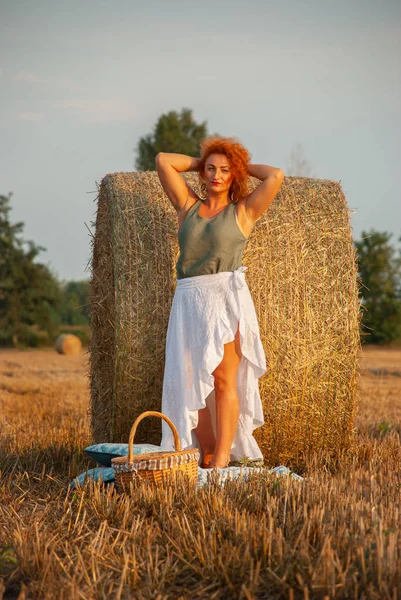 Roodharige vrouw poseren op het veld in de buurt van een stapel hooi — Stockfoto