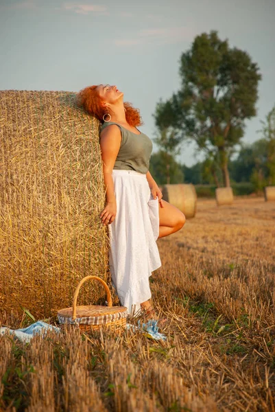 Donna dai capelli rossi in posa sul campo vicino a una pila di fieno — Foto Stock