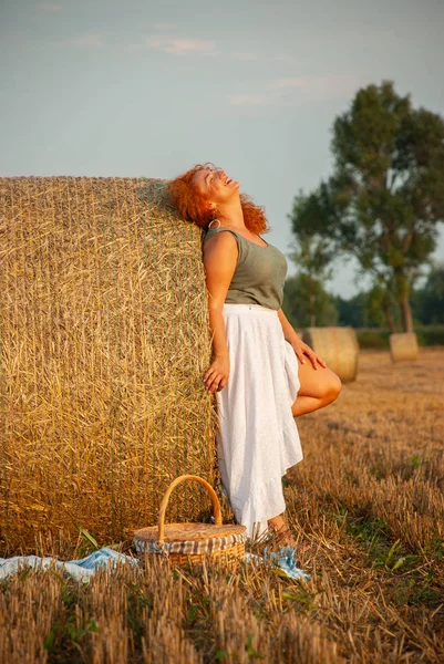 Roodharige vrouw poseren op het veld in de buurt van een stapel hooi — Stockfoto
