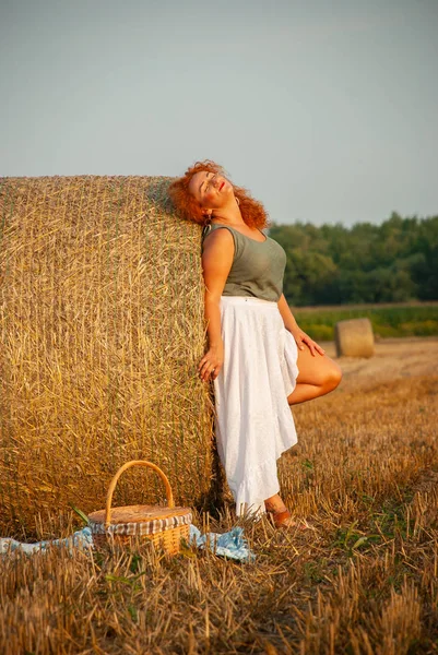 Roodharige vrouw poseren op het veld in de buurt van een stapel hooi — Stockfoto