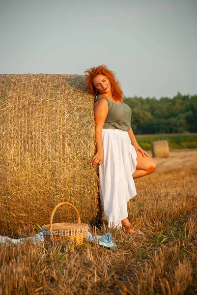 Red-haired woman posing on the field near a hay stack — Stock Photo, Image