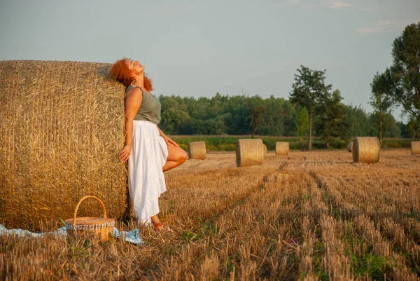 Red-haired woman posing on the field near a hay stack — Stock Photo, Image