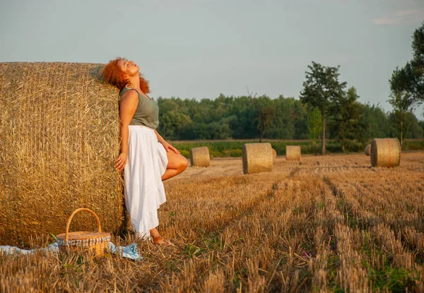 Red-haired woman posing on the field near a hay stack — Stock Photo, Image