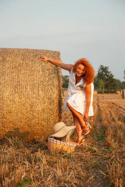 Donna dai capelli rossi in posa sul campo vicino a una pila di fieno — Foto Stock