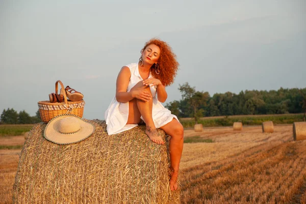 Red-haired woman posing on the field near a hay stack — Stock Photo, Image