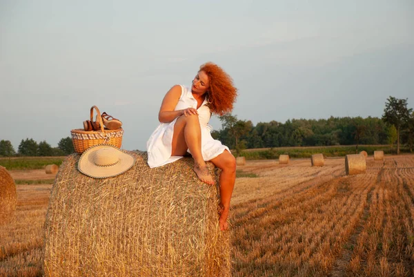 Roodharige vrouw poseren op het veld in de buurt van een stapel hooi — Stockfoto