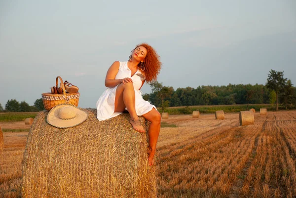 Roodharige vrouw poseren op het veld in de buurt van een stapel hooi — Stockfoto