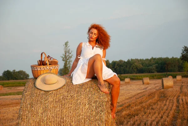 Donna dai capelli rossi in posa sul campo vicino a una pila di fieno — Foto Stock