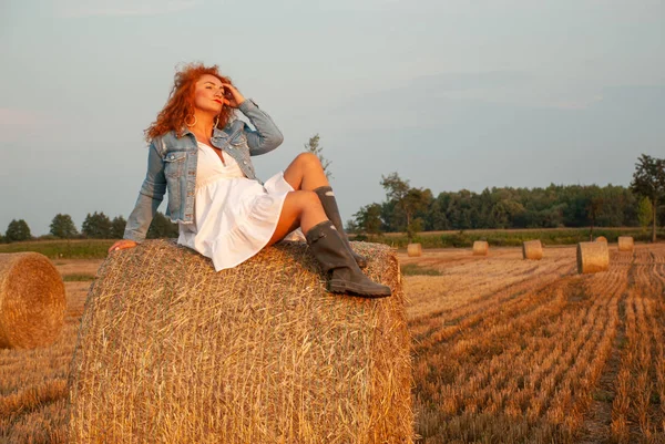 Рудоволоса жінка позує на полі біля стопки сіна — стокове фото